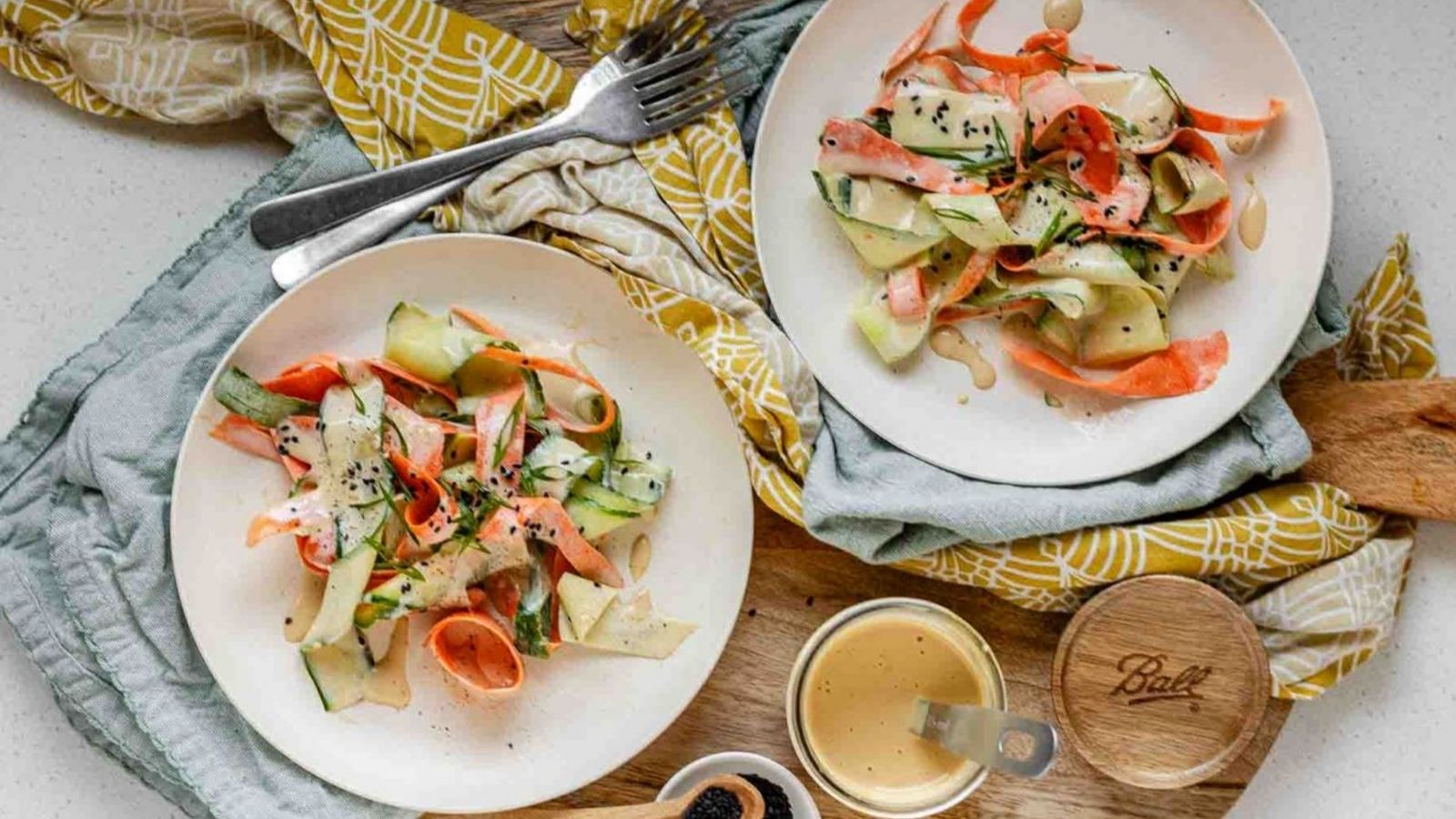 Ribbons of cucumber and carrot on a plate topped with dressing and black sesame seeds.