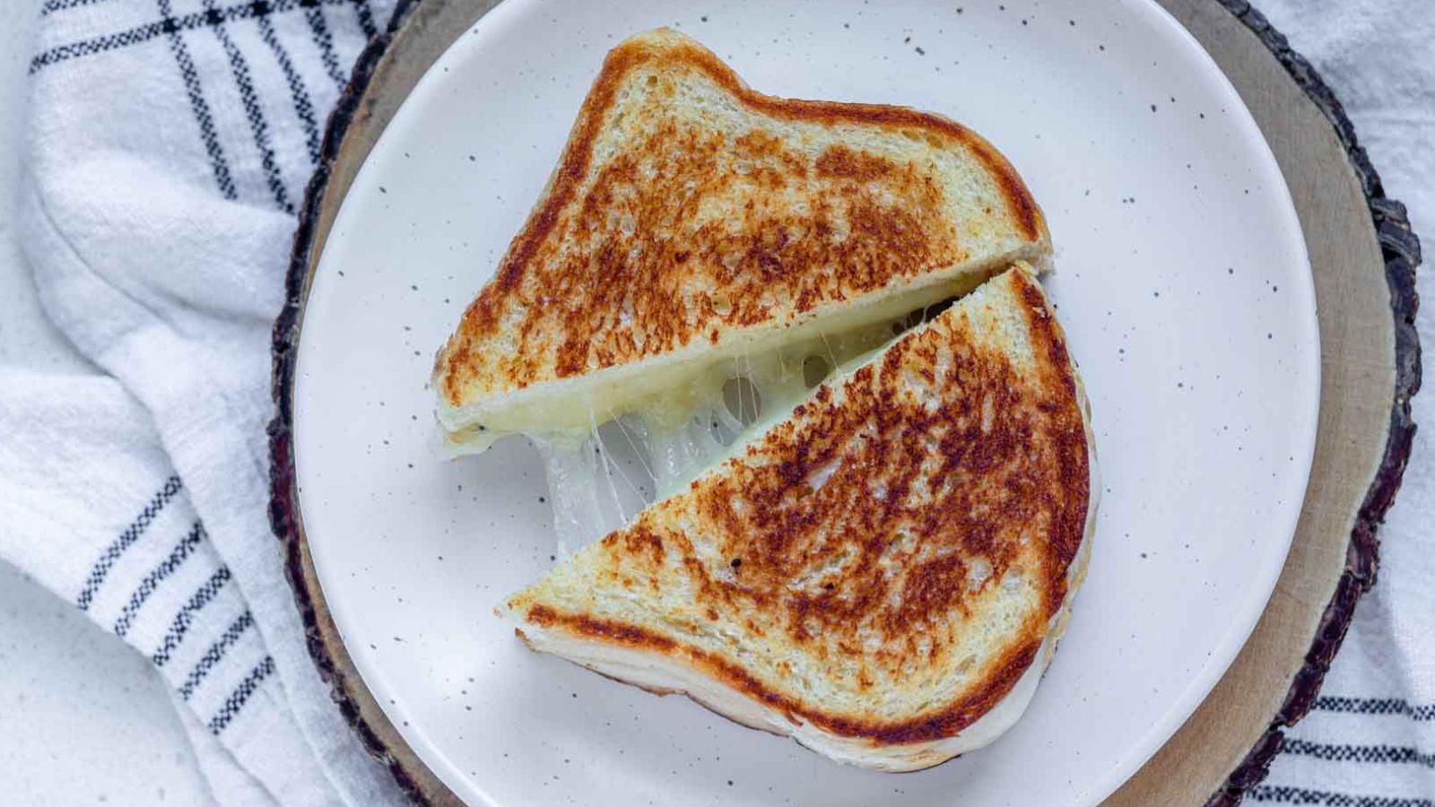 A grilled cheese sandwich on a plate with melty cheese between the halves.