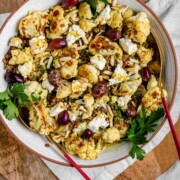 A large serving bowl with roasted cauliflower, black olives, lentils, feta cheese, slivered almonds, and fresh parsley.