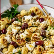 A large serving bowl with roasted cauliflower, black olives, lentils, feta cheese, slivered almonds, and fresh parsley.