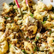 A large serving bowl with roasted cauliflower, black olives, lentils, feta cheese, slivered almonds, and fresh parsley with the text roasted cauliflower lentil salad.