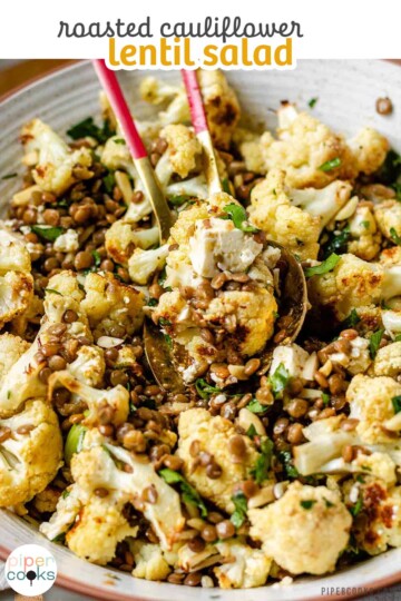 A large serving bowl with roasted cauliflower, black olives, lentils, feta cheese, slivered almonds, and fresh parsley with the text roasted cauliflower lentil salad.