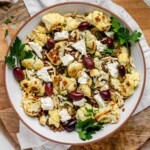 A large serving bowl with roasted cauliflower, black olives, lentils, feta cheese, slivered almonds, and fresh parsley.