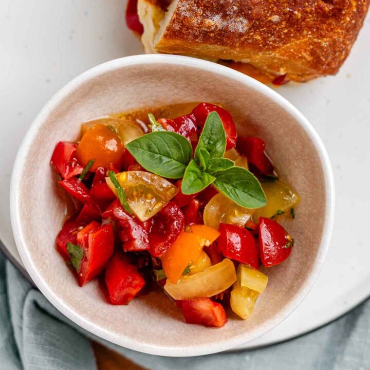 A bowl of chopped tomatoes with fresh oregano leaves.