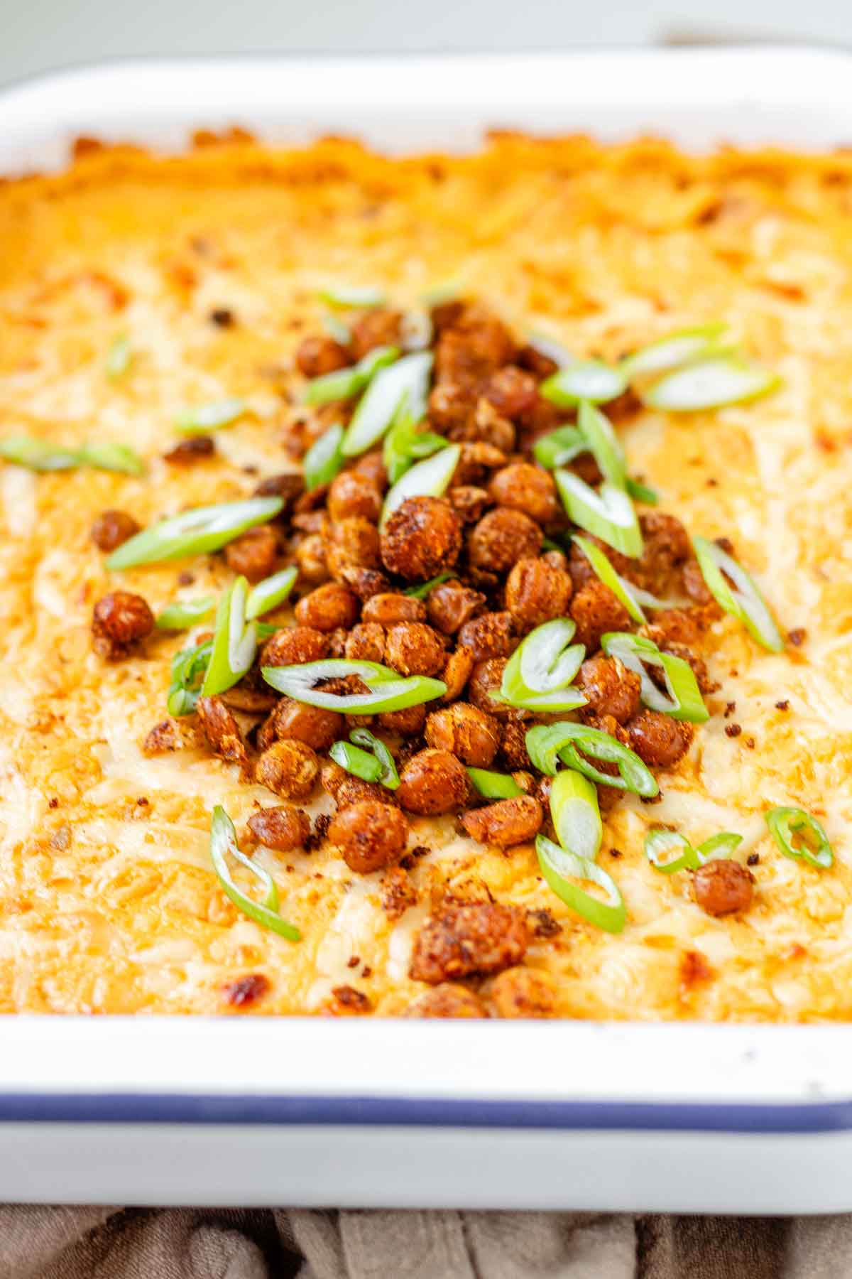 Golden baked buffalo chickpea dip fresh from the oven with melted cheese and pan-fried crispy chickpeas on top.