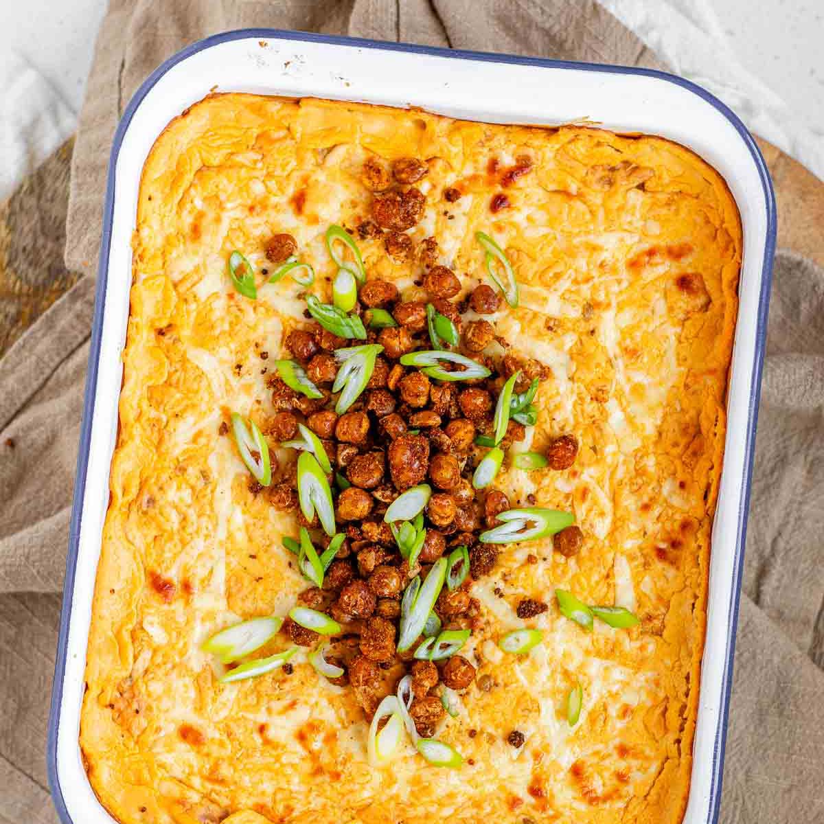 Golden baked buffalo chickpea dip fresh from the oven with melted cheese and pan-fried crispy chickpeas on top.