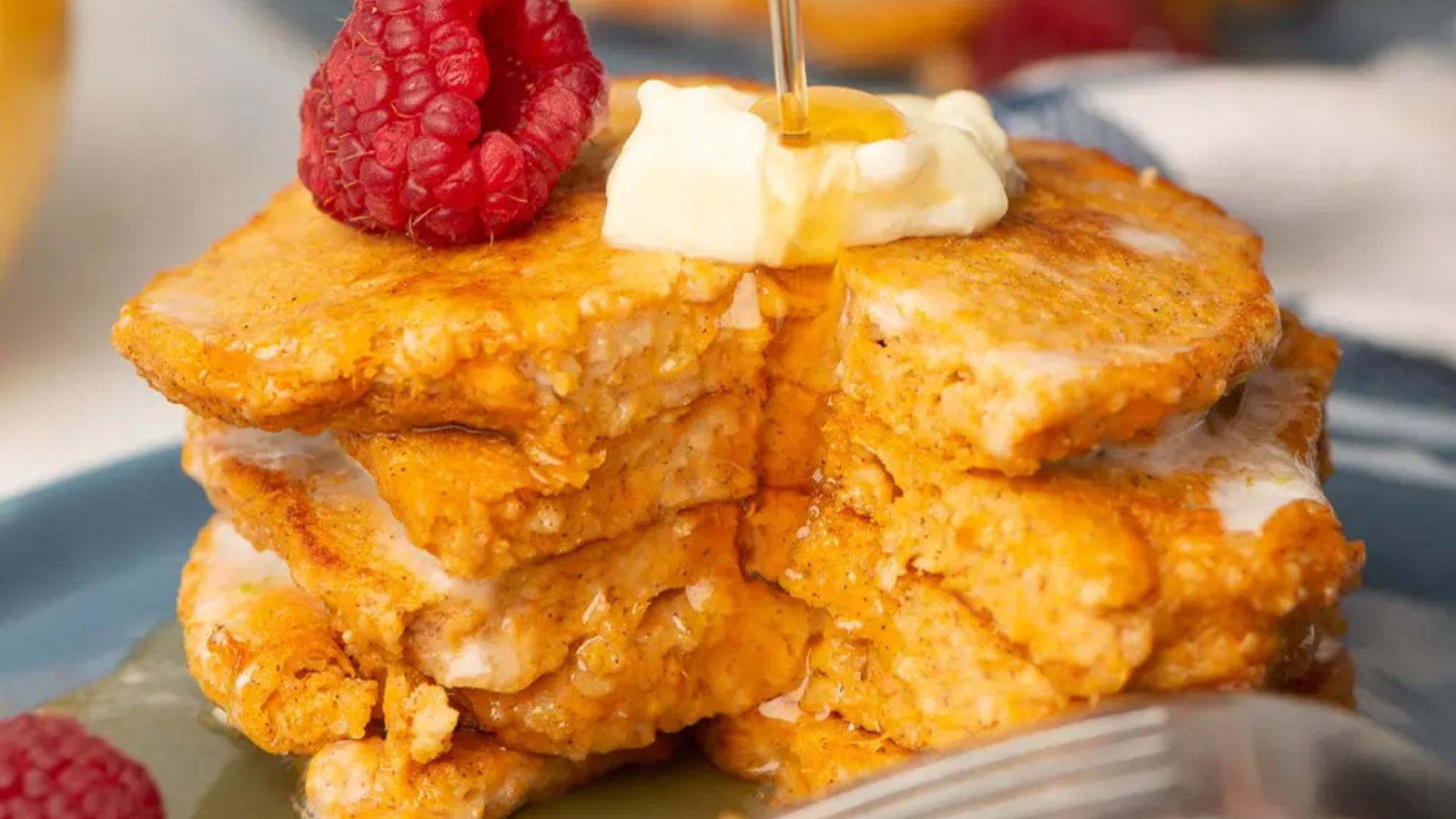 A stack of sweet potato pancakes topped with butter, syrup and a raspberry.