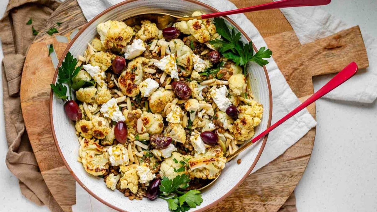 Cauliflower salad in a bowl topped with olives, cheese, and almond slivers.