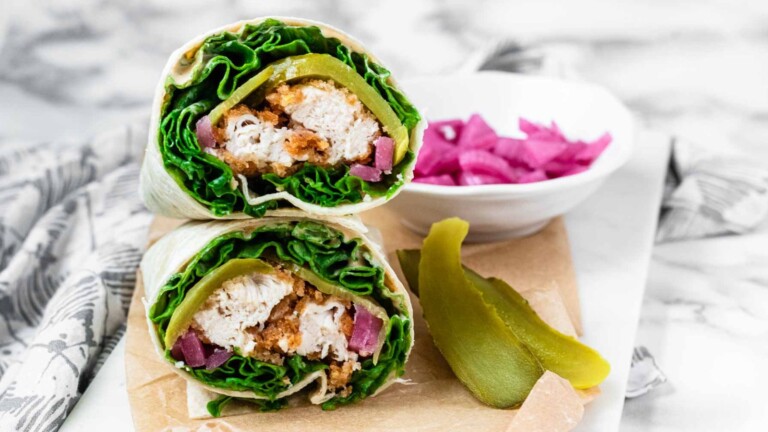 A chicken, lettuce, pickle, and pickled red onion wrap sliced in half and stacked.