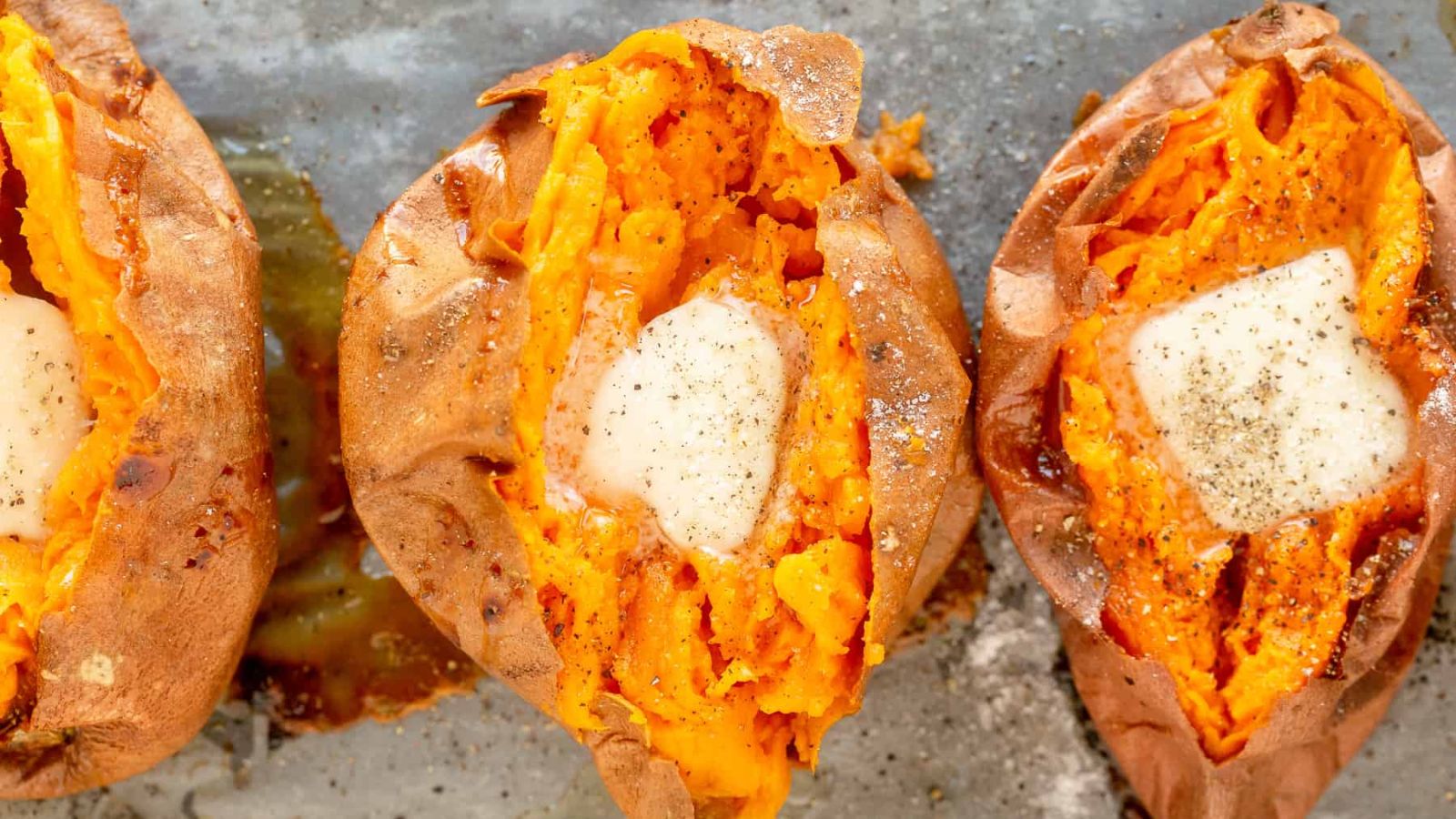Three baked sweet potatoes sliced open and topped with butter.
