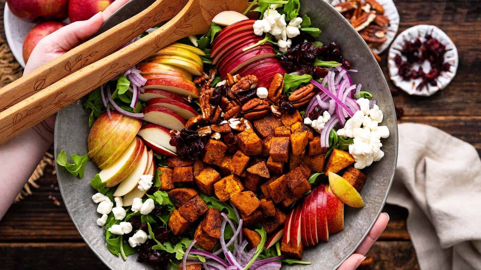 A salad with sweet potato cubes, greens, sliced apples, white cheese, and nuts.