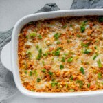 A rice casserole in a baking dish topped with melted cheese and sliced green onions.