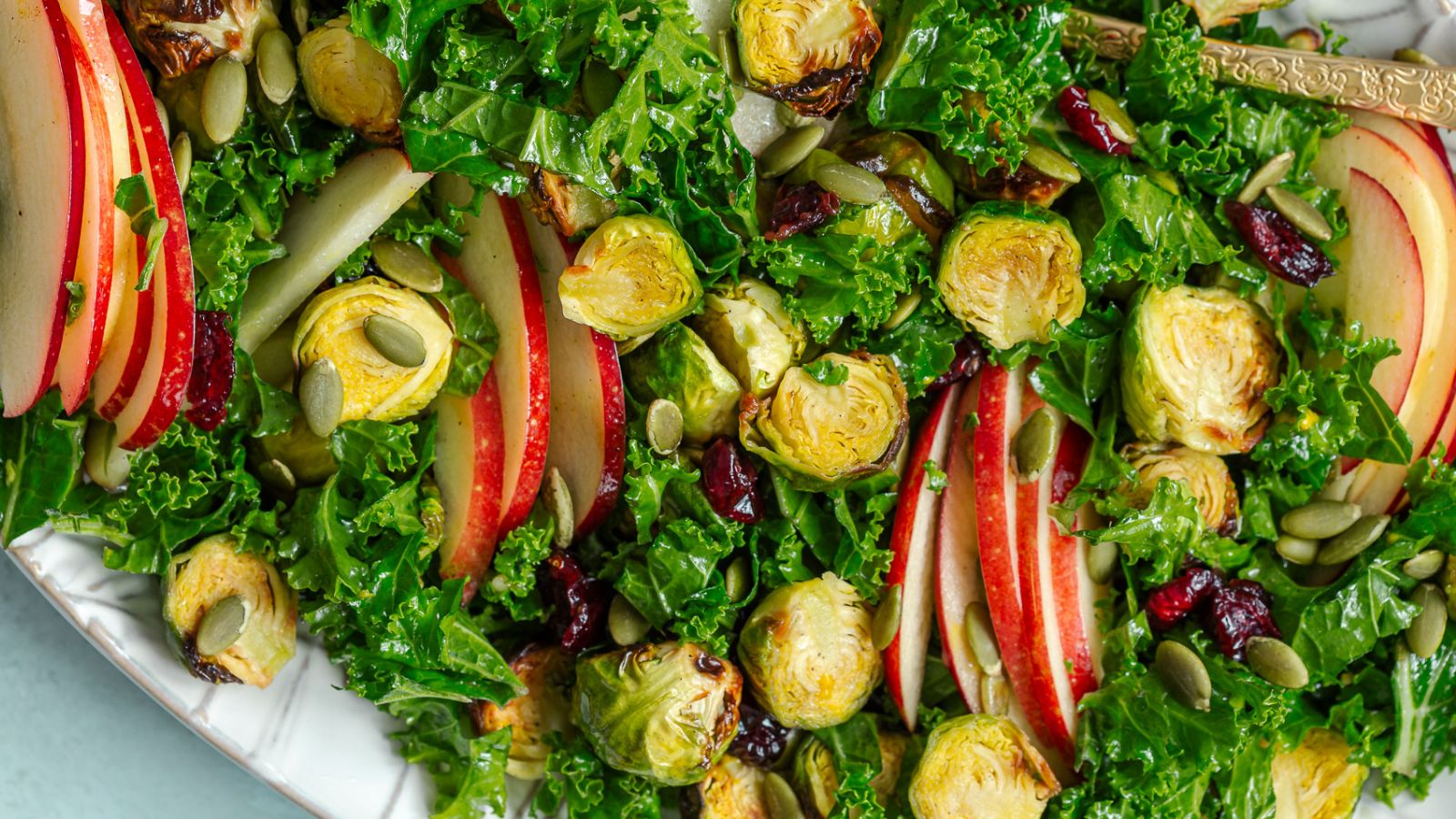 A salad with green, Brussels sprouts, and sliced apples.