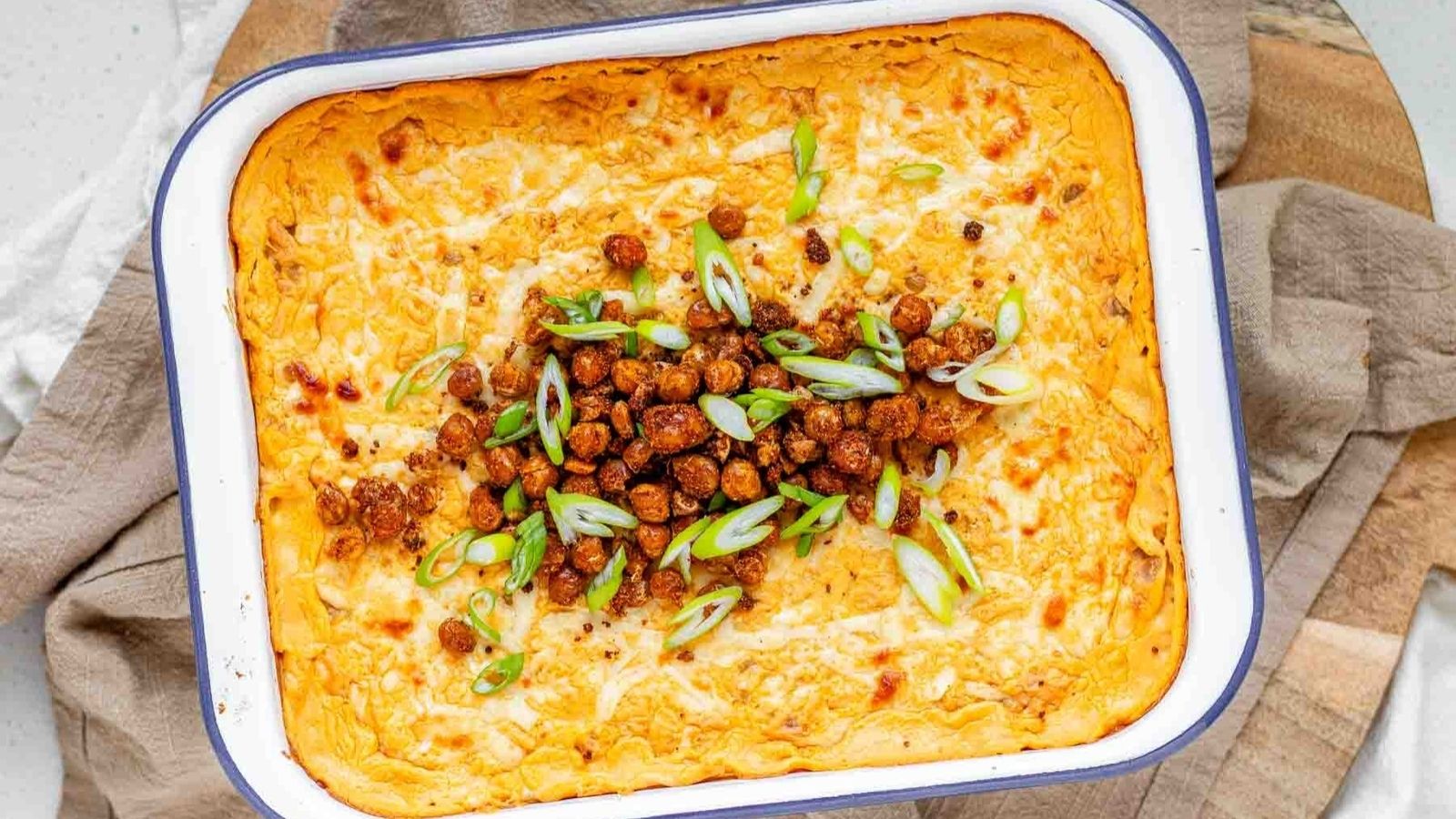 Golden baked buffalo chickpea dip fresh from the oven with melted cheese and pan-fried crispy chickpeas on top.