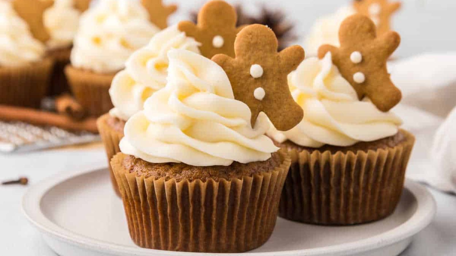 Gingerbread cupcakes on a white plate topped with white icing and gingerbread men cookies.