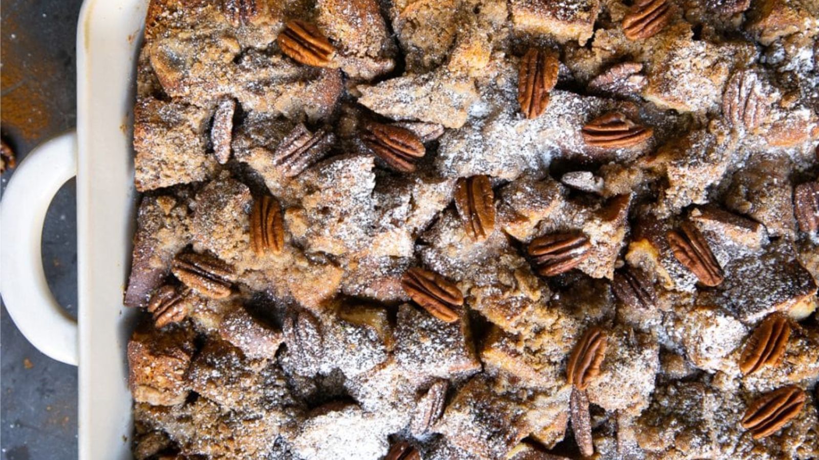 A breakfast bake topped with pecans and powdered sugar.