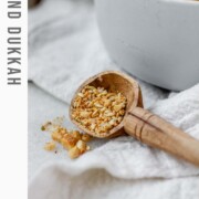 Close-up of homemade almond dukkah in a small bowl, showing toasted almonds, sesame seeds, and spices with the text almond dukkah.