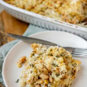 Baked rice and artichoke casserole topped with melted Havarti and Parmesan cheese in a white dish and a plate.