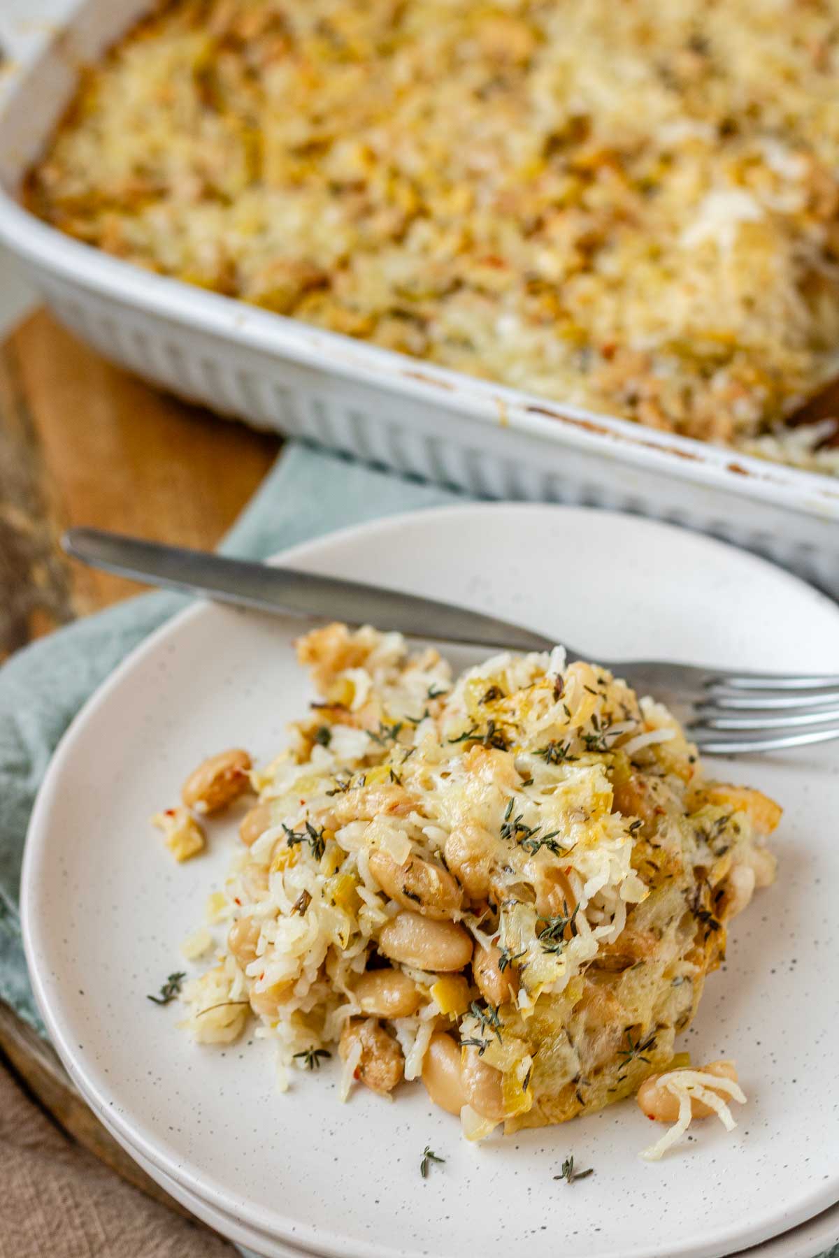 Baked rice and artichoke casserole topped with melted Havarti and Parmesan cheese in a white dish and a plate.