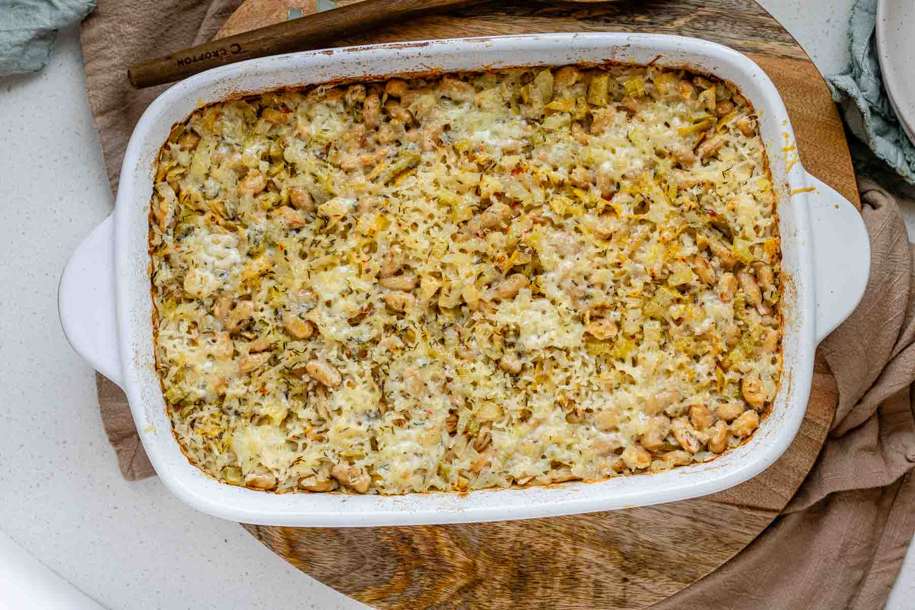 Baked rice and artichoke casserole topped with melted Havarti and Parmesan cheese in a white dish.