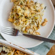 Baked rice and artichoke casserole topped with melted Havarti and Parmesan cheese in a white dish and a plate.