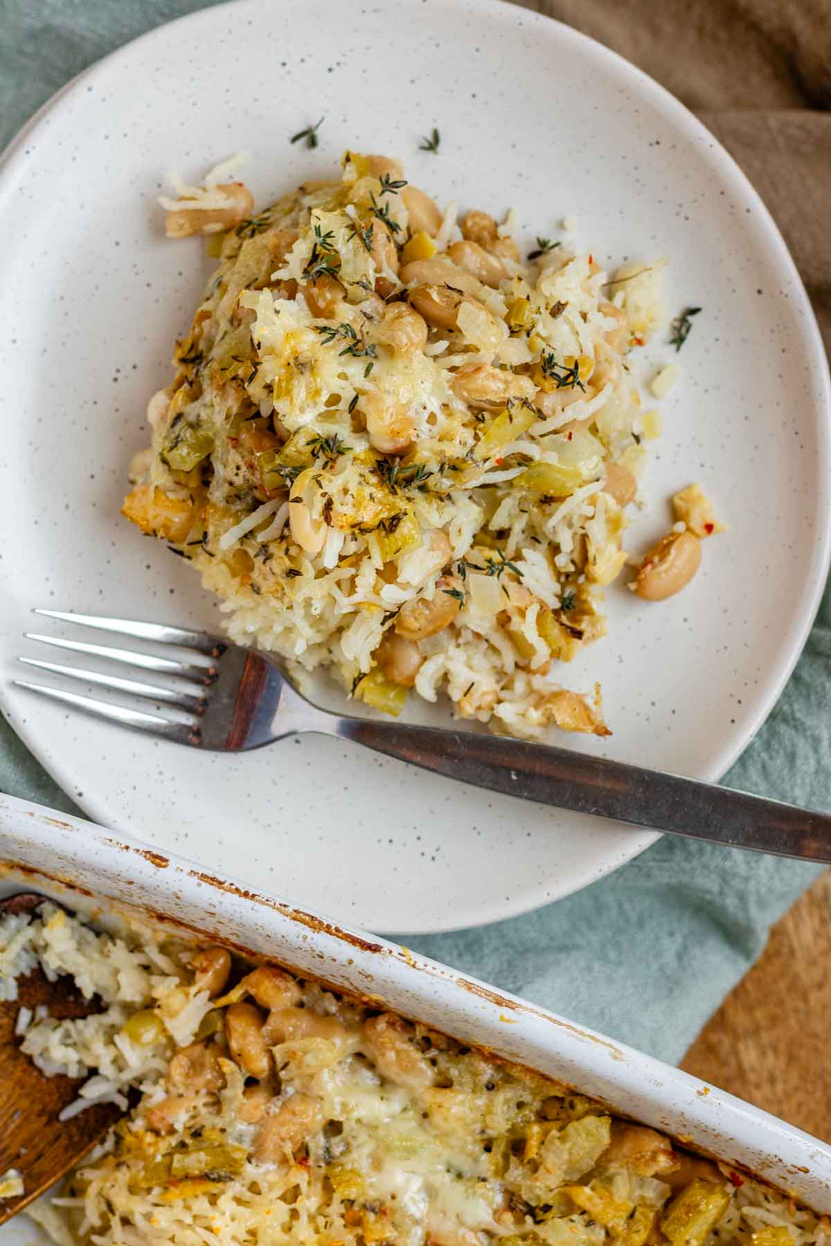 Baked rice and artichoke casserole topped with melted Havarti and Parmesan cheese in a white dish and a plate.