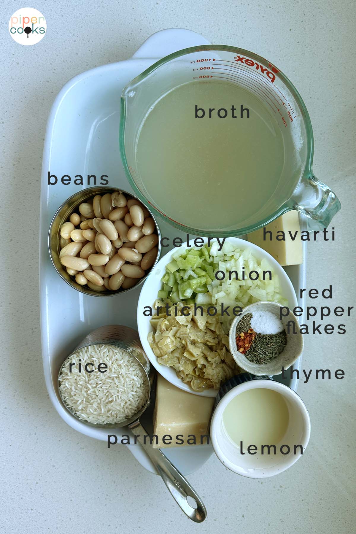 Ingredients laid out for a casserole, labeled with the text broth, beans, celery, havarti, onion, artichoke, red pepper flakes, thyme, rice, parmesan, and lemon.