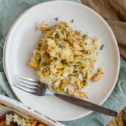 Baked rice and artichoke casserole topped with melted Havarti and Parmesan cheese in a white dish and a plate with the text artichoke casserole with rice.