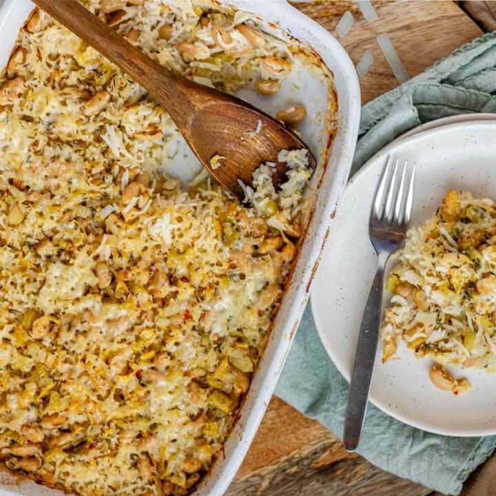 Baked rice and artichoke casserole topped with melted Havarti and Parmesan cheese in a white dish and a plate.