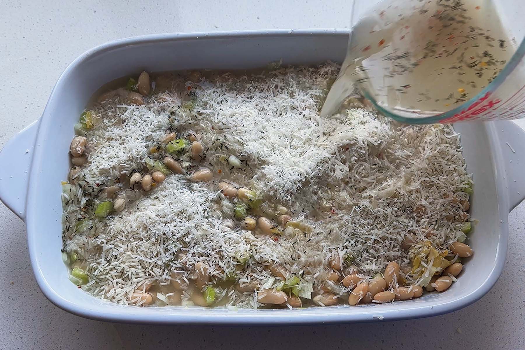 Hot lemon-thyme broth being poured into the rice and artichoke casserole before covering with foil.