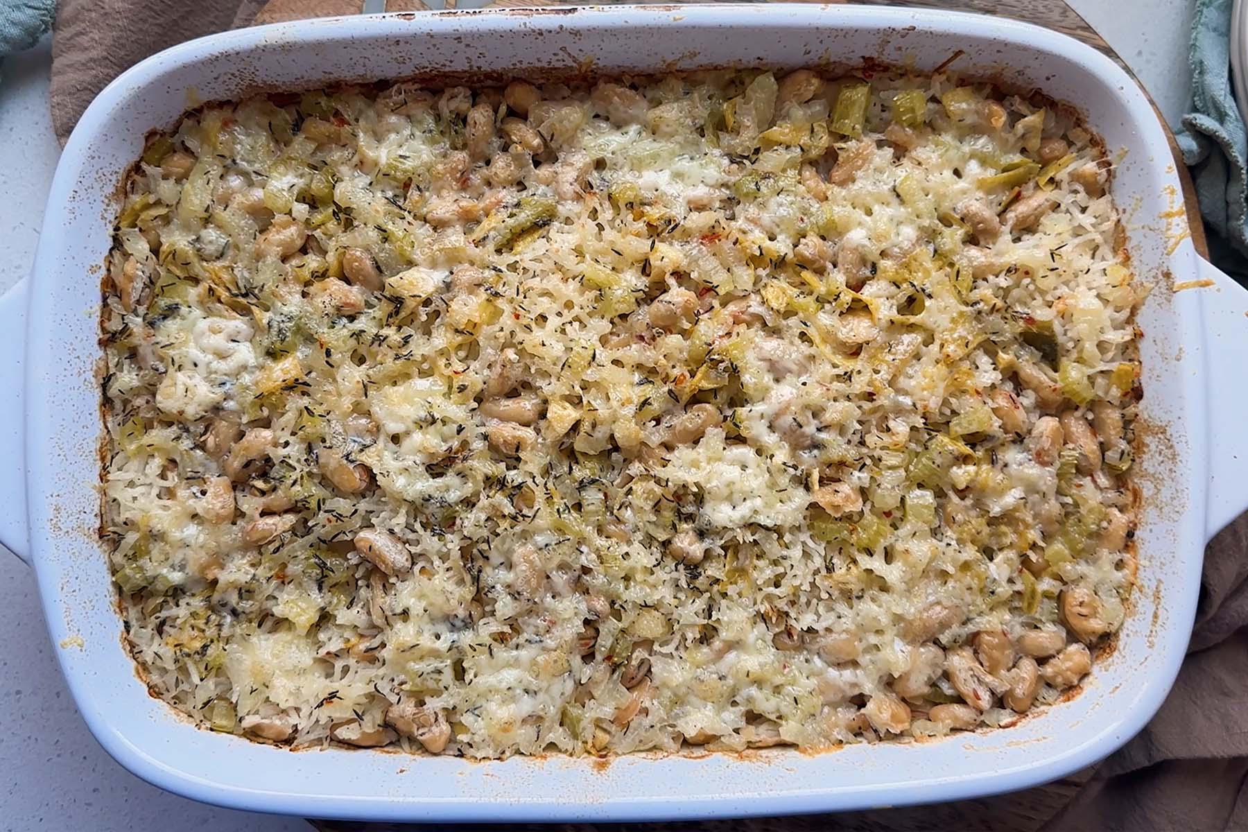 Baked rice and artichoke casserole topped with melted Havarti and Parmesan cheese in a white dish.