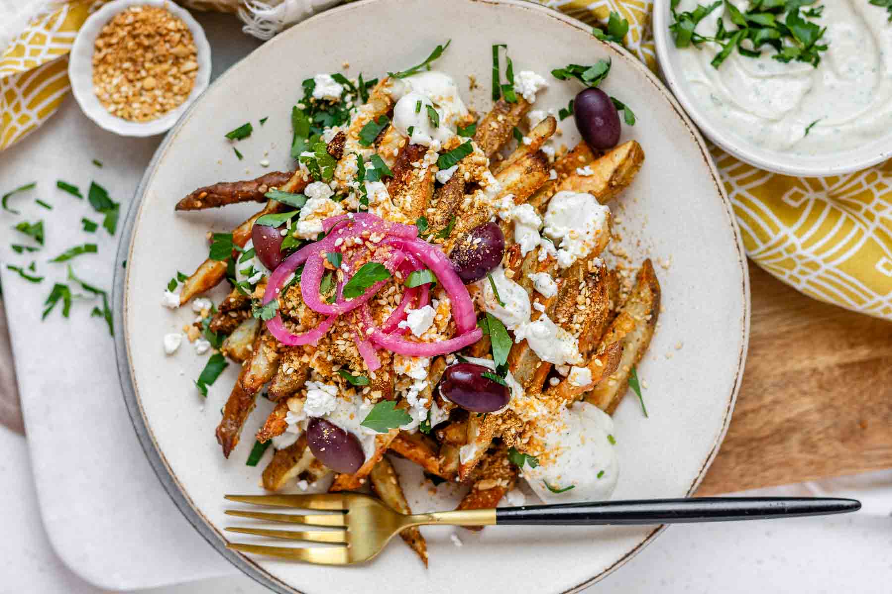 Crispy homemade Dukkah Fries served with tahini yogurt sauce, feta, olives, and pickled red onions.