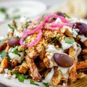 Close-up of golden Dukkah-coated fries with tahini yogurt sauce, feta, olives, and pickled red onions.