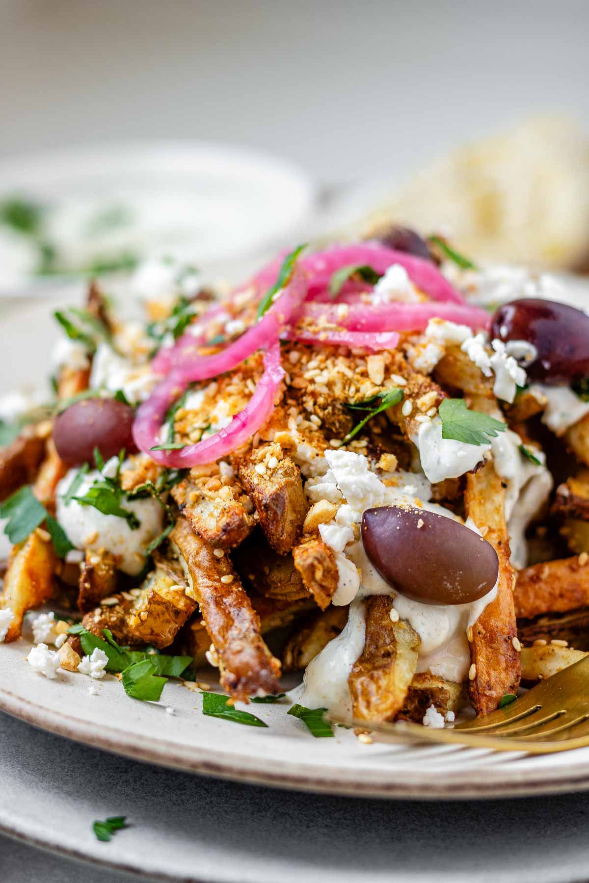 Close-up of golden Dukkah-coated fries with tahini yogurt sauce, feta, olives, and pickled red onions.