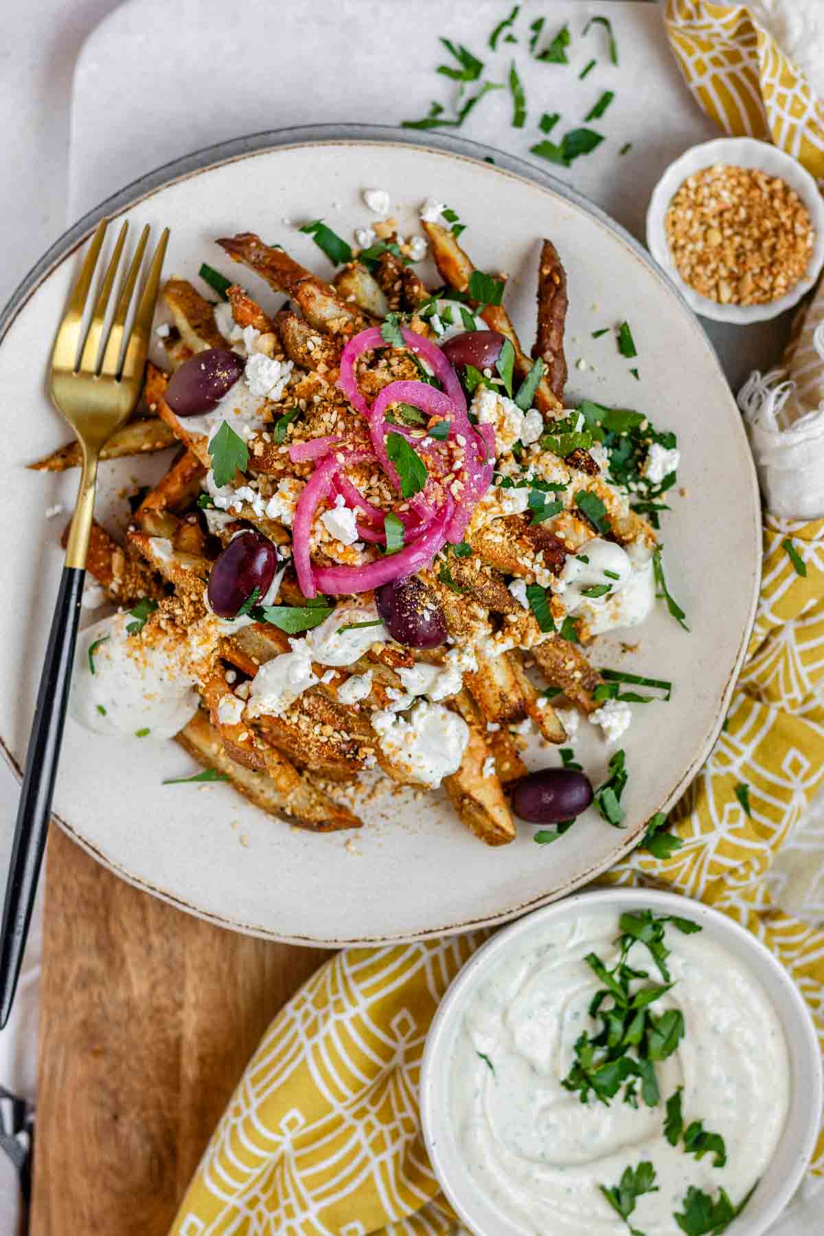 Crispy homemade Dukkah Fries served with tahini yogurt sauce, feta, olives, and pickled red onions.