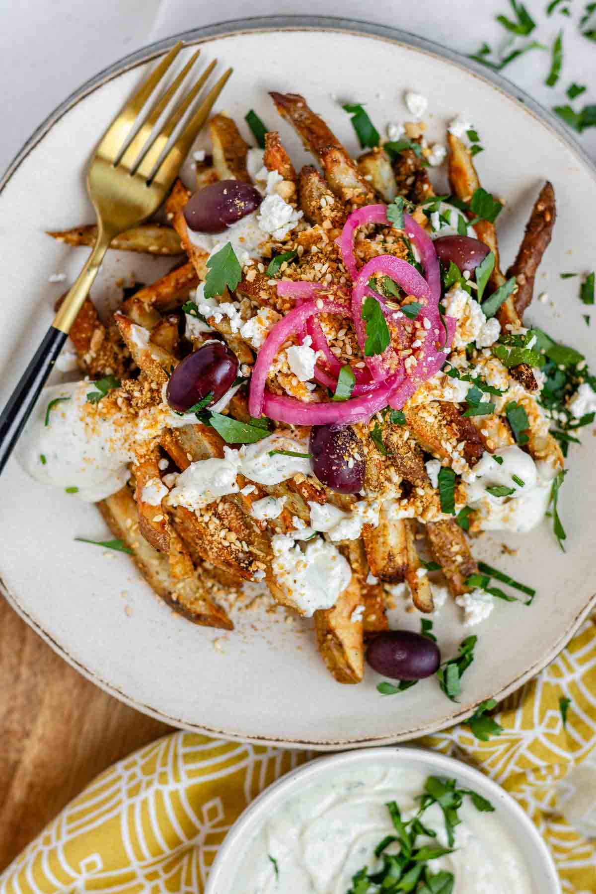 Crispy homemade Dukkah Fries served with tahini yogurt sauce, feta, olives, and pickled red onions.
