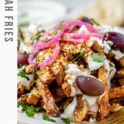 Crispy homemade Dukkah Fries served with tahini yogurt sauce, feta, olives, and pickled red onions with the text Dukkah Fries.