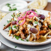 Crispy homemade Dukkah Fries served with tahini yogurt sauce, feta, olives, and pickled red onions with the text Dukkah Fries.