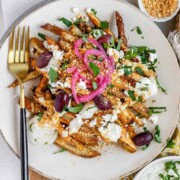 Crispy homemade Dukkah Fries served with tahini yogurt sauce, feta, olives, and pickled red onions with the text Dukkah Fries.