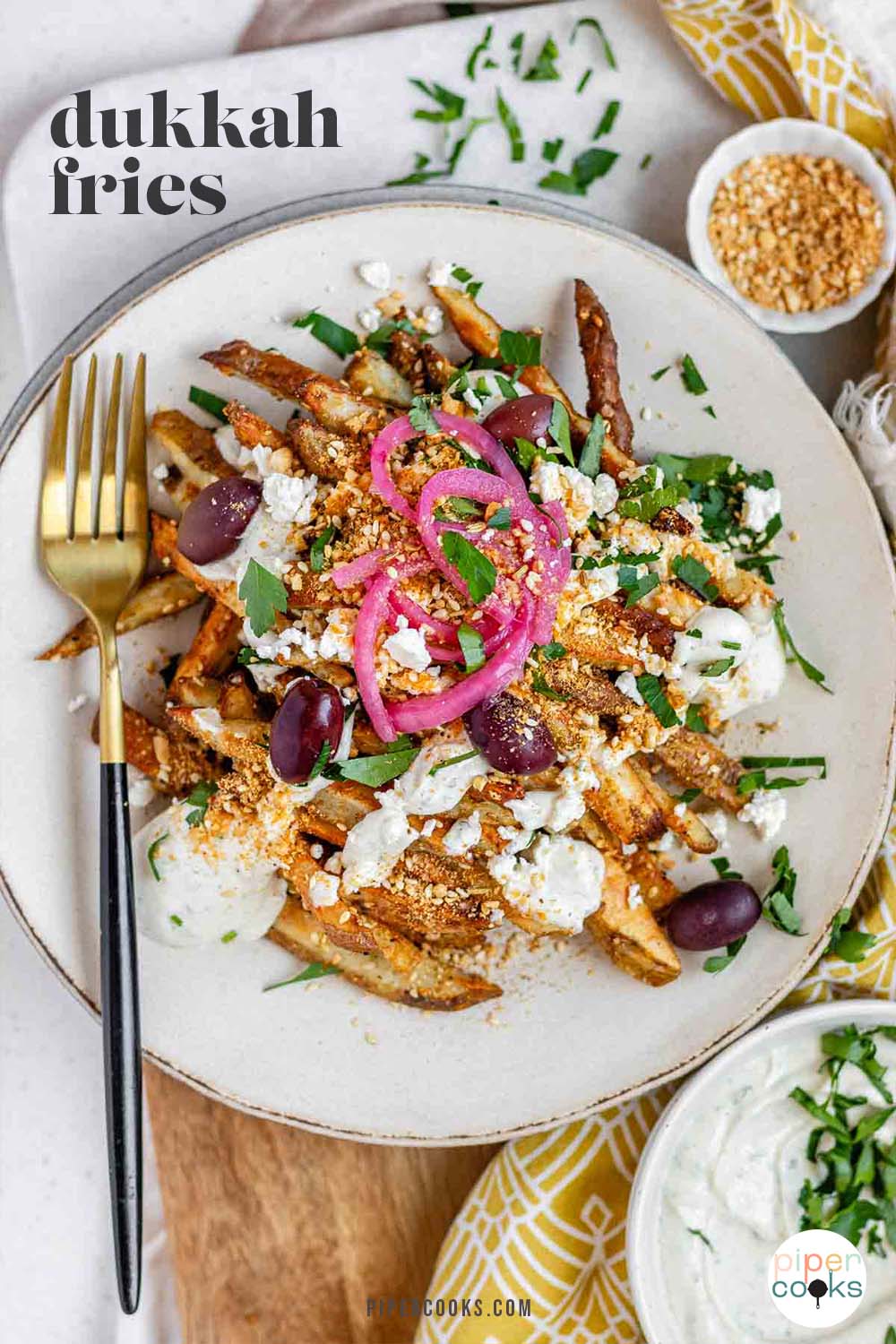 Crispy homemade Dukkah Fries served with tahini yogurt sauce, feta, olives, and pickled red onions with the text Dukkah Fries.