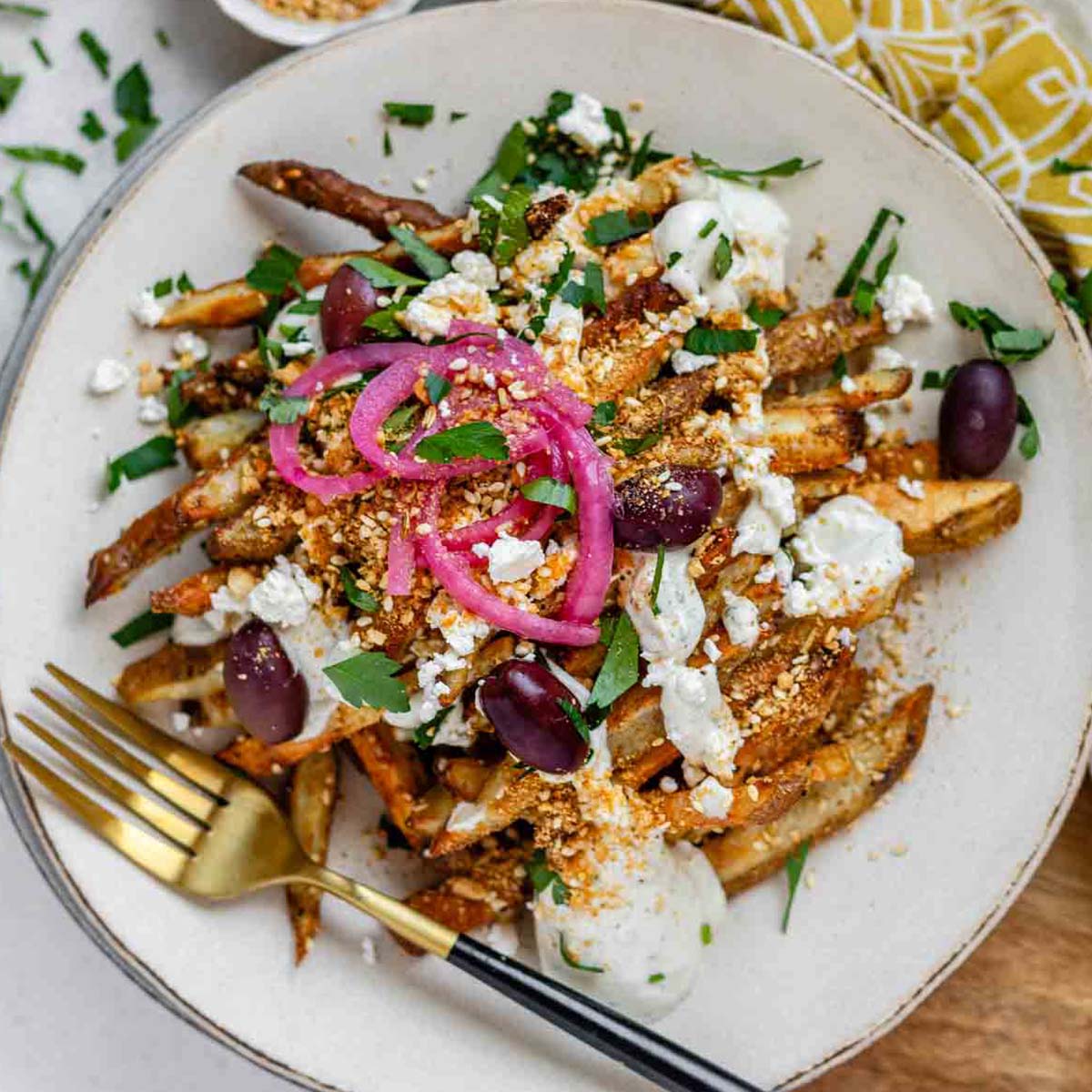 Crispy homemade Dukkah Fries served with tahini yogurt sauce, feta, olives, and pickled red onions.