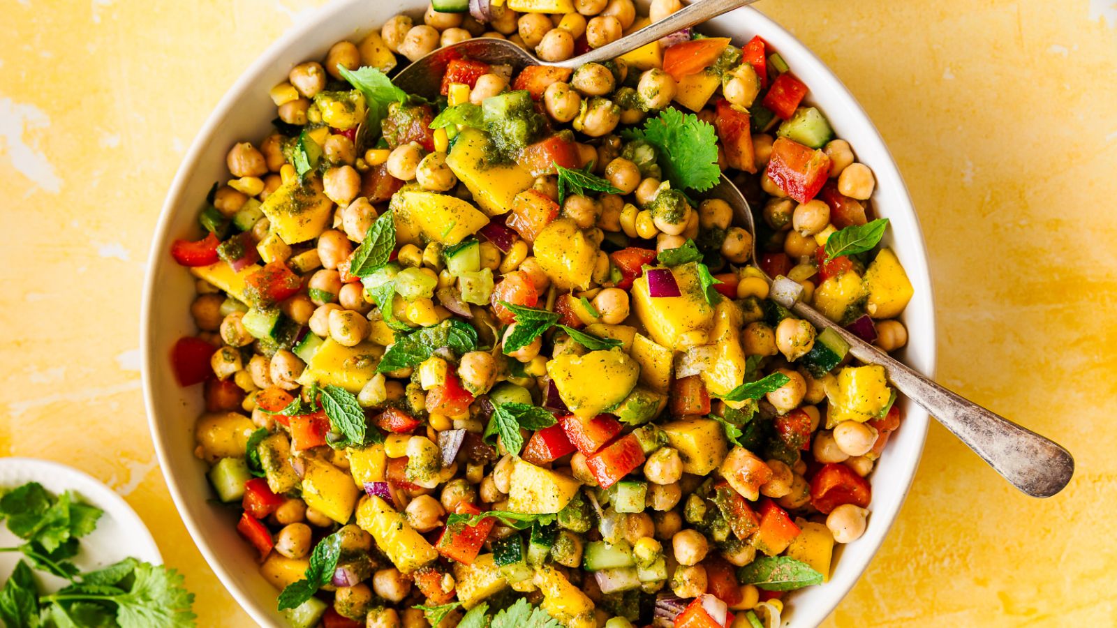 A bowl of mango chickpea salad with bell pepper, cucumber, and herbs.