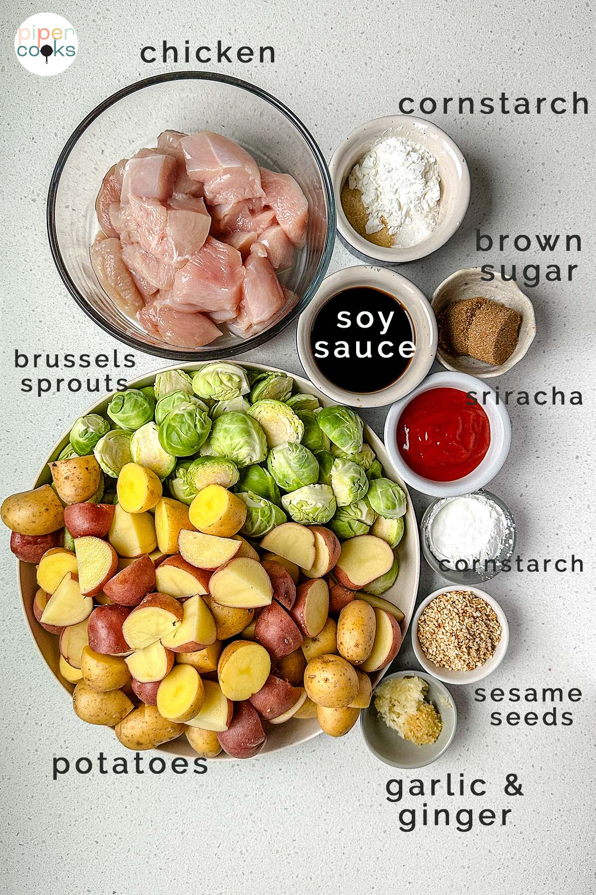Ingredients laid out for spicy sesame chicken: raw chicken cubes, Brussels sprouts, potatoes, sriracha, soy sauce, and sesame seeds, all labeled with text.