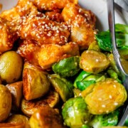 Plated serving of spicy sesame chicken, baby potatoes, and Brussels sprouts..