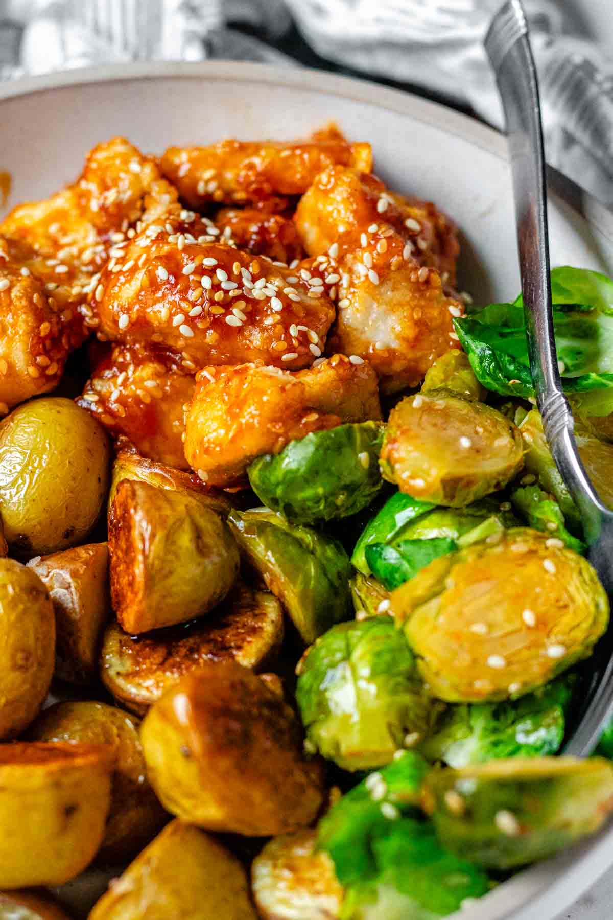 Plated serving of spicy sesame chicken, baby potatoes, and Brussels sprouts..