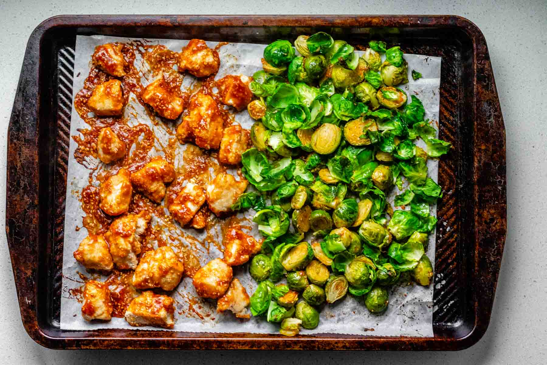 Sheet pan with spicy sesame chicken and roasted Brussels sprouts drizzled with sesame sauce.