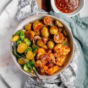 Plated serving of spicy sesame chicken, baby potatoes, and Brussels sprouts with extra sesame sauce on the side with text sheet pan sesame chicken potatoes & brussels.