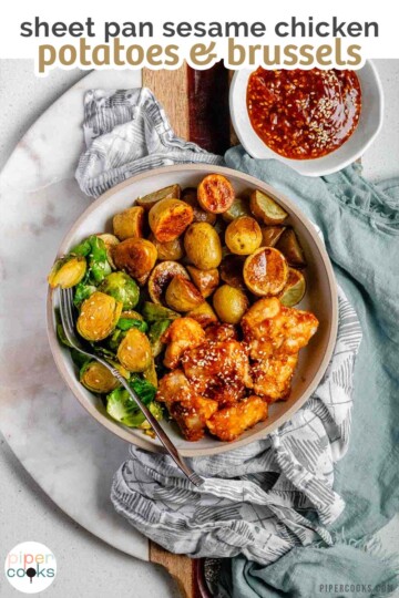 Plated serving of spicy sesame chicken, baby potatoes, and Brussels sprouts with extra sesame sauce on the side with text sheet pan sesame chicken potatoes & brussels.