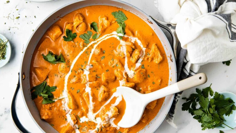 Butter chicken with a yogurt drizzle and cilantro leaves in a pan.