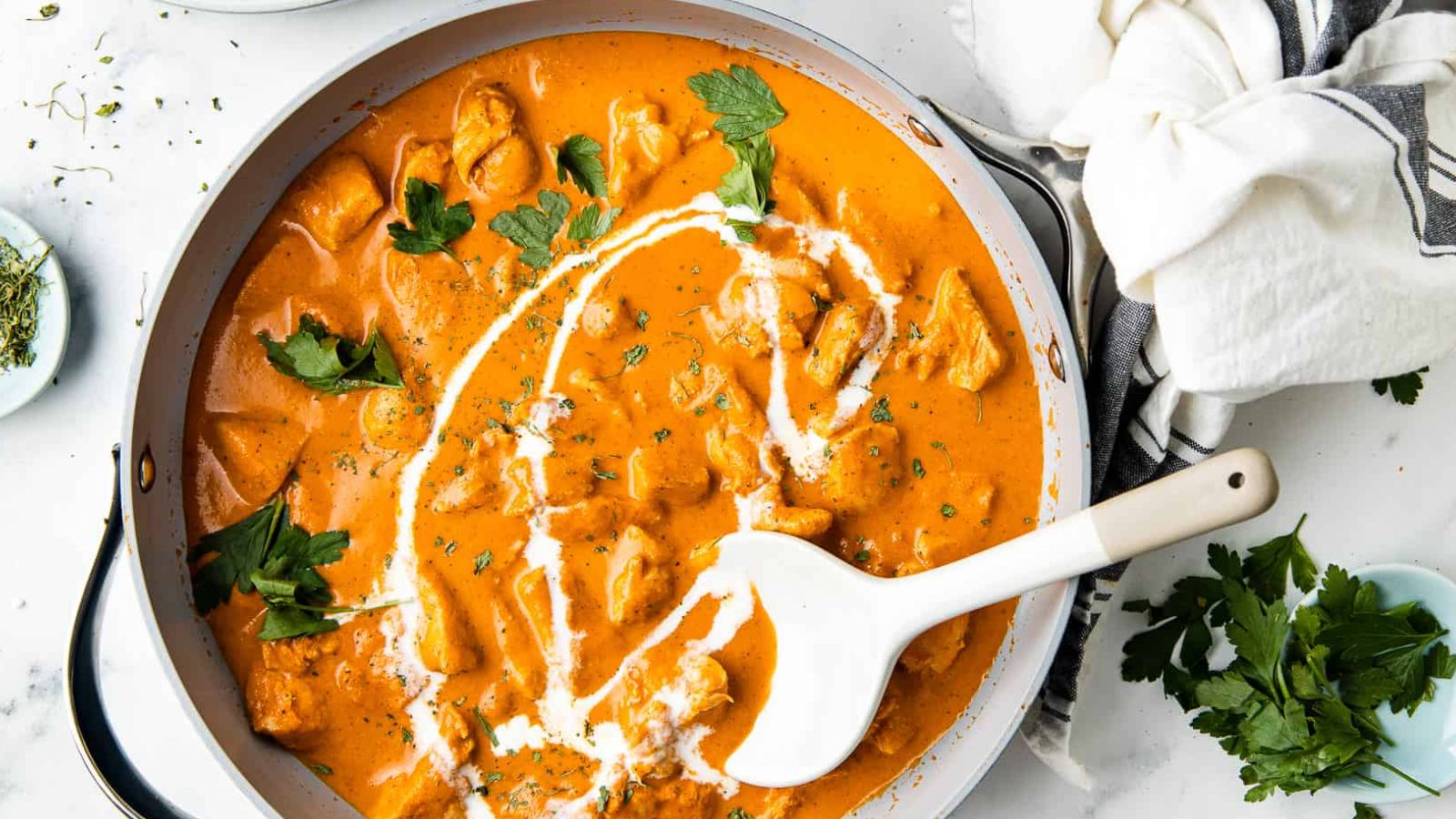 Butter chicken with a yogurt drizzle and cilantro leaves in a pan.